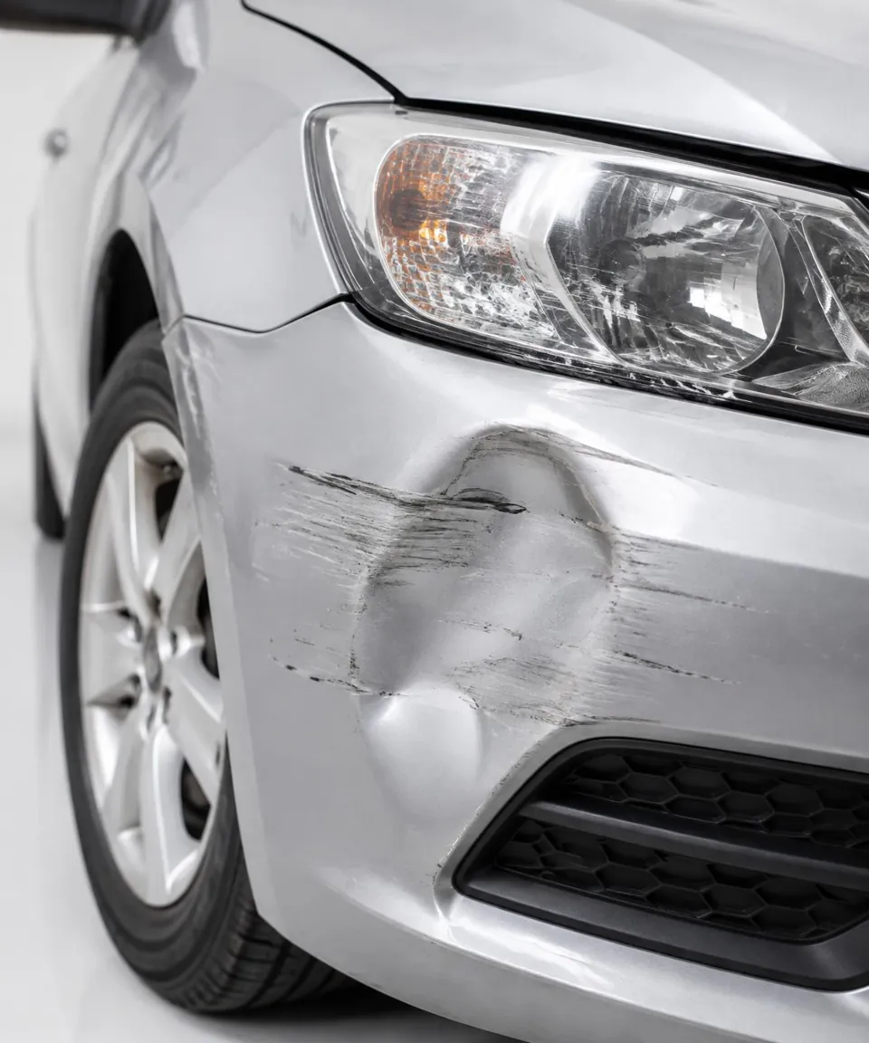 Eingedrückter Stoßfänger an einem silbernen Fahrzeug nach einem Unfall – Symbolbild